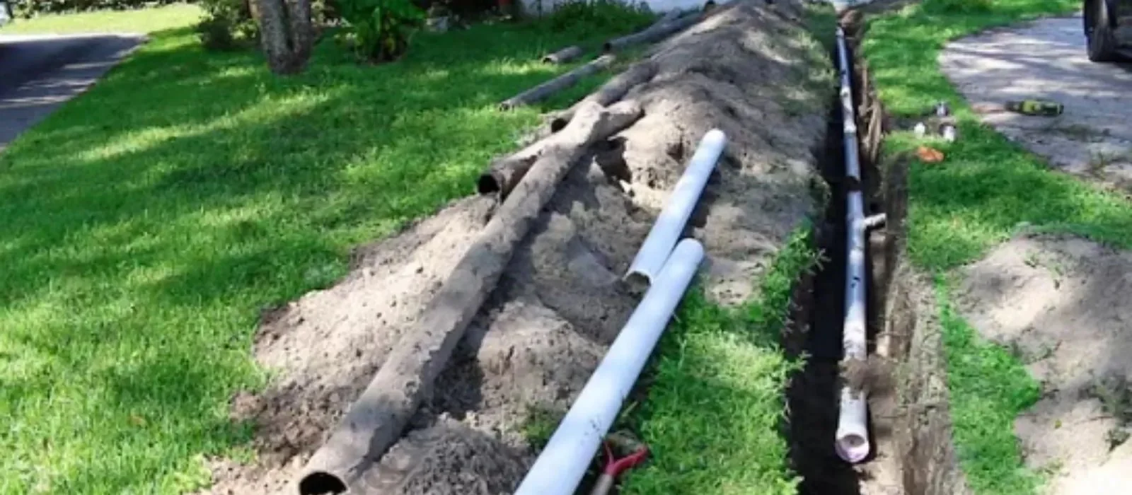 Old cast iron sewer pipe lying beside new PVC pipe in an open trench on a Pennsauken, NJ lawn